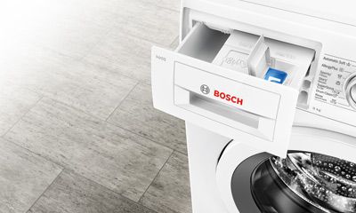 Waschturm mit Waschmaschine und Trockner vor gestreifter Wand. Daneben ein schwarzer Tisch mit gefaltetem Handtuchstapel. Waschturm mit Waschmaschine und Trockner vor gestreifter Wand. Daneben ein schwarzer Tisch mit gefaltetem Handtuchstapel.